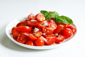 red cherry tomato and basil leaf on white plate on white background