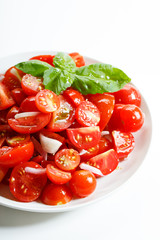red cherry tomato and basil leaf on white plate on white background