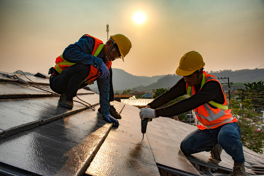 The roof work team in work clothes and special protective gloves using air guns or air nails and install asphalt or tar on the new roof under the residential building.