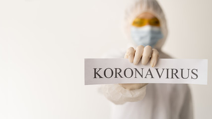 a woman in a special protective bone holds a sheet with the text coronavirus in her hands. The...