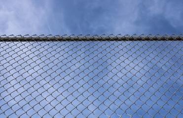 Looking up at a chain link fence with blue sky and clouds.