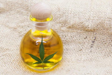 Marijuana seed oil in the glass bottle with the marijuana leaf on the marijuana fabric