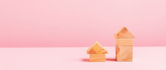 Houses big and small of wooden cubes on a pink background. The concept of building houses from environmentally friendly