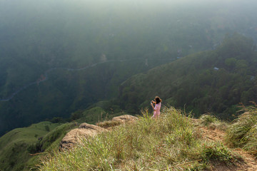 Obraz premium Girl enjoys a mountain view while standing on a cliff