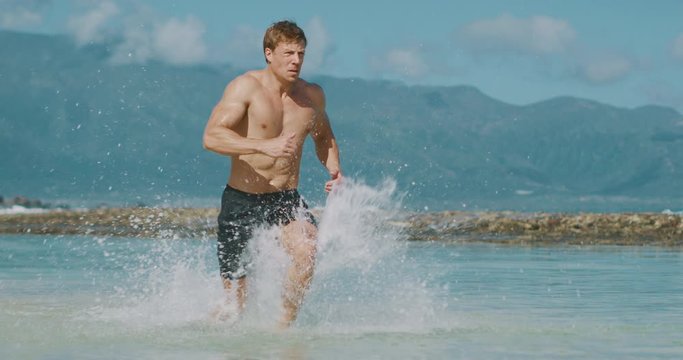 Young attractive muscular man running on the beach in slow motion, baywatch body, beach workout run