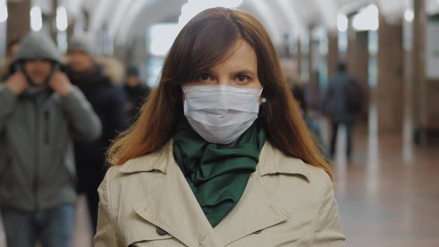 Young Woman Wear Face Protective Mask Looking At Camera, Closeup. Moving Crowd Of People Blurred In Motion In Background, Timelapse