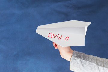 Hand holds a paper airplane. On the airplane, the inscription "COVID- 19". The concept of the spread of the coronovirus around the world.