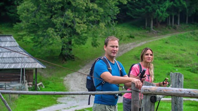 An active couple opening a fence and leaving their wooden hut accommodation to hike in the woods