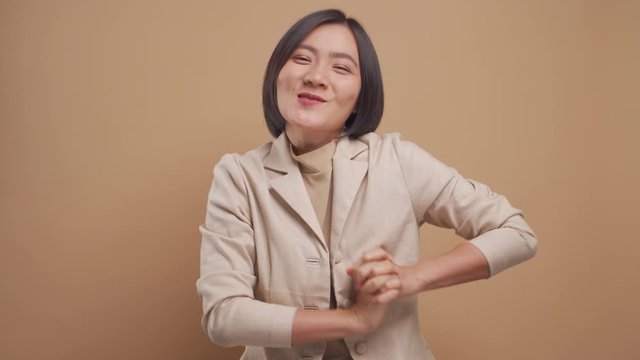 Happy asian business woman feel shy standing isolated over beige background. 4K video