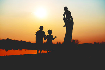 Fototapeta na wymiar Silhouette of a family comprising a father, mother and two children happy family the sunset.Concept of friendly 