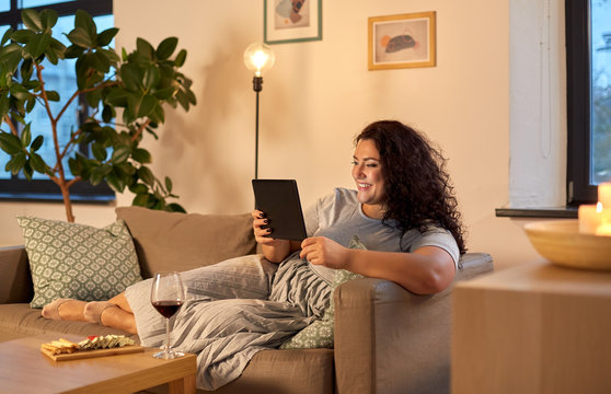 technology, leisure and people concept - happy smiling woman with tablet pc computer, red wine and snacks at home in evening