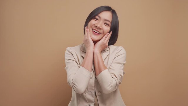 Happy asian business woman feel shy standing isolated over beige background. 4K video