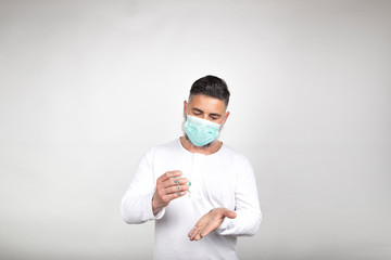 Man with surgical mask uses a disinfectant to clean his hands of germs on white background. Coronavirus prevention concept. Epidemic