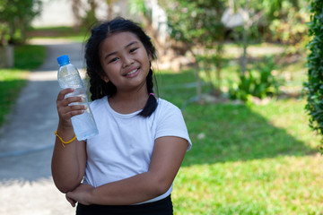 An Asian girl with a hair wearing a white shirt. Standing smiling in the garden, his right hand holding a bottle of clean drinking water On a sunny and hot day