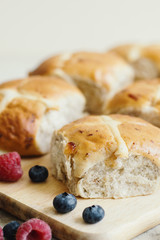 Hot cross buns served on wooden board with fresh berries. Traditional Easter treats. Homemade pastry