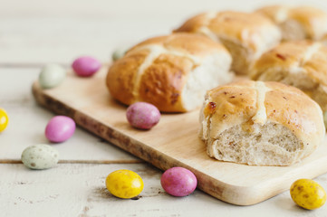 Hot cross buns served on a wooden board and small chocolate eggs. Easter treats. Festive season