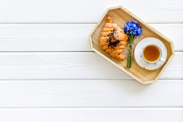 Breakfast with summer flowers. Tea, croissant and cornflowers on white wooden background top-down copy space