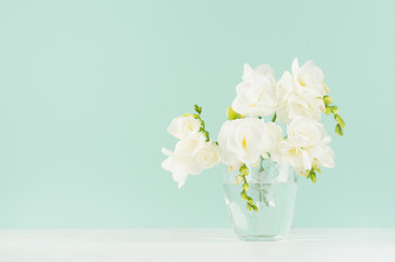 Beautiful fresh spring white flowers freesia in gentle glass in green mint menthe interior on white wood board as fresh season background.