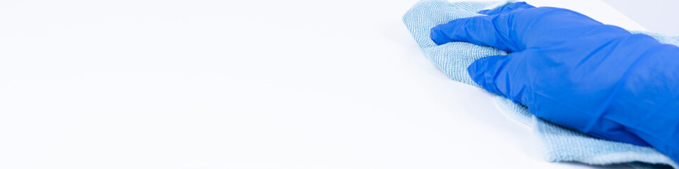 A hand with blue nitirl gloves cleaning a white surface