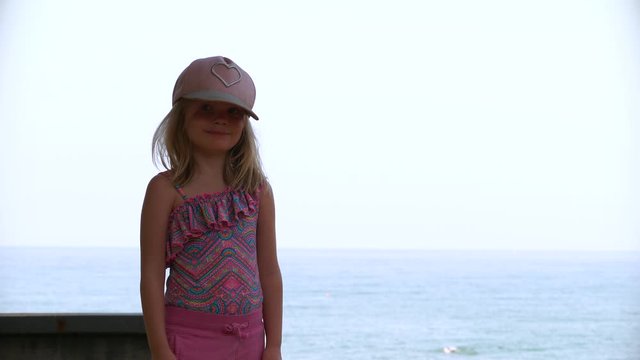Portrait of blonde child girl with sun hat and sea in background. Static