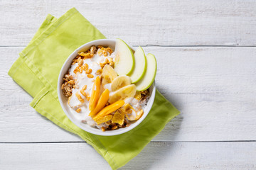 Granola and vegetarian yogurt with slices of apple, apricot, banana on a white wooden background. Healthy breakfast concept. Top view, copy space