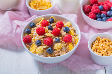 Yogurt, bowls with granola, blueberries and raspberries, cornflakes and puffed rice on a white wooden background. Healthy breakfast