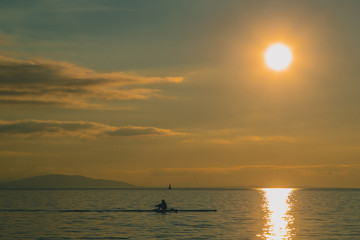 Kayaker or a person in a paddle boat on a lake during evening hours. Romantic leisure activity on the water. Sun about to set into the water.