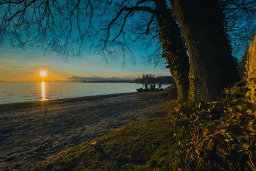 Romantic evening on the shores of Lac Leman at a beach at Lausanne. Sun just setting down in the lake during winter time in Lausanne.
