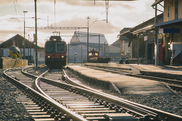 Train station in switzerland, frontal view of the train and train tracks in strong evening sunset...