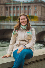 Young woman sitting in front of the Swedish parliament building in Stockholm on a dull autumn day.
