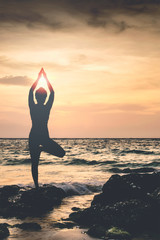 Silhouette of woman doing yoga with seascape and sunset backgound.