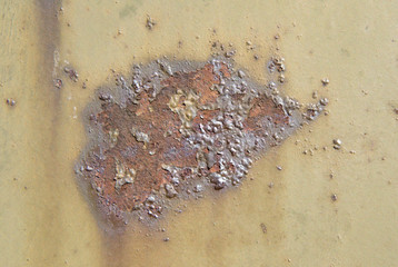 A stain of brown rust on a khaki-colored metal surface. Bubble-blown corrosion.