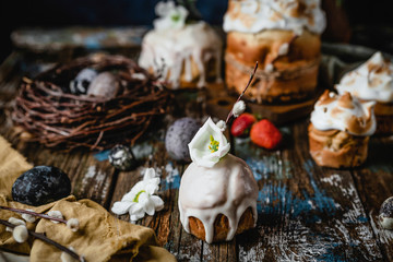 Variety of Easter cakes on wooden table with dyed eggs, berries and flowers on dark blue background, festive table setting, selective focus