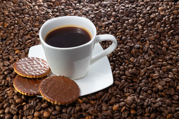 White cup of hot coffee on a background of brown beans.