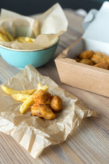 Delicious Chicken nuggets and French fries on a wooden background in craft packaging