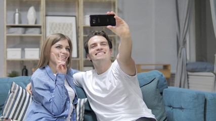 Young Couple Taking Selfie with Smartphone while Sitting on Couch