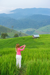 Asian woman taking photo of rice field with mountain background