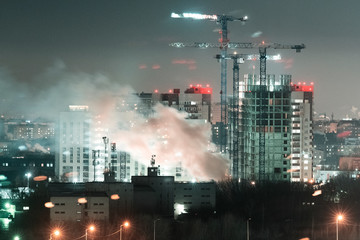Tower cranes, the construction of a new tall apartment building at a construction site in the city at night time. Development, construction industry concept