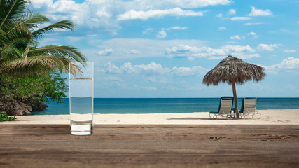 Pure morning. Glass of cold mineral water on the table of the beach background with palms and sand. Chilled refreshing drink. Concept of summertime, vacation, resort, weekend, healthy lifestyle.
