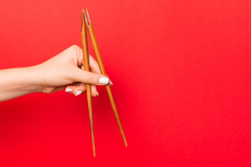 Wooden chopsticks holded with female hands on red background. Ready for eating concepts with empty...