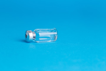 Closeup vaccine bottle on blue isolated background. No inscription, blank for advertising.