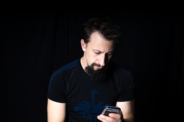 a man with a beard on a dark background looks at the phone