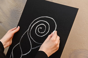 a shell drawn on a black chalk Board and a hand with a bar of chalk
