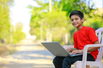 Cute little Indian/Asian boy studying or playing game with laptop computer