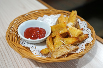 A wooden basket of potato wedge fries with tomato ketchup