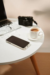 Office desk with mobile phone, coffee cup, laptop, camera and glasses