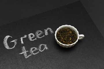 green tea leaves in a mug on the background of a black board with the inscription