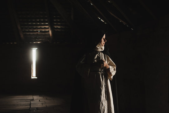 Catholic nun prays in the dark old church. Historical cosplay of vintage church. A woman in old nun catholic cassock