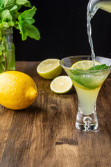 Top view of jar serving a mojito in glass with lime slice and mint on wooden table and black background in vertical
