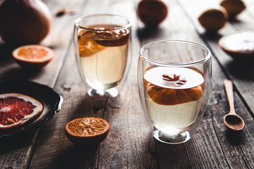 Citrus tea in a transparent teapot and a glass, healthy drink on a wooden background.